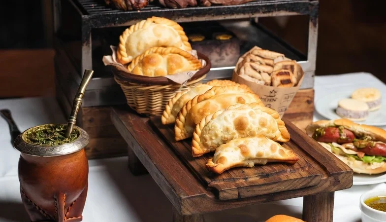 Traditional Argentine foods including asado, empanadas, choripán, alfajores, and mate served on a rustic dining table.